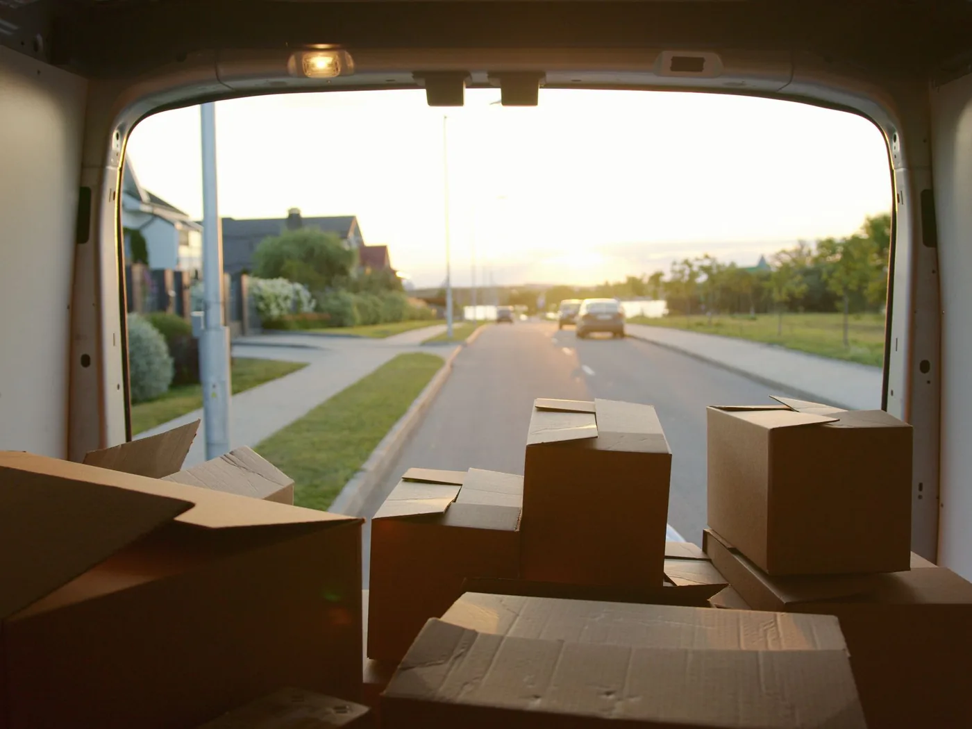 Uitzicht vanuit een geladen bestelbus met verhuisdozen op een rustige woonstraat aan het einde van de dag